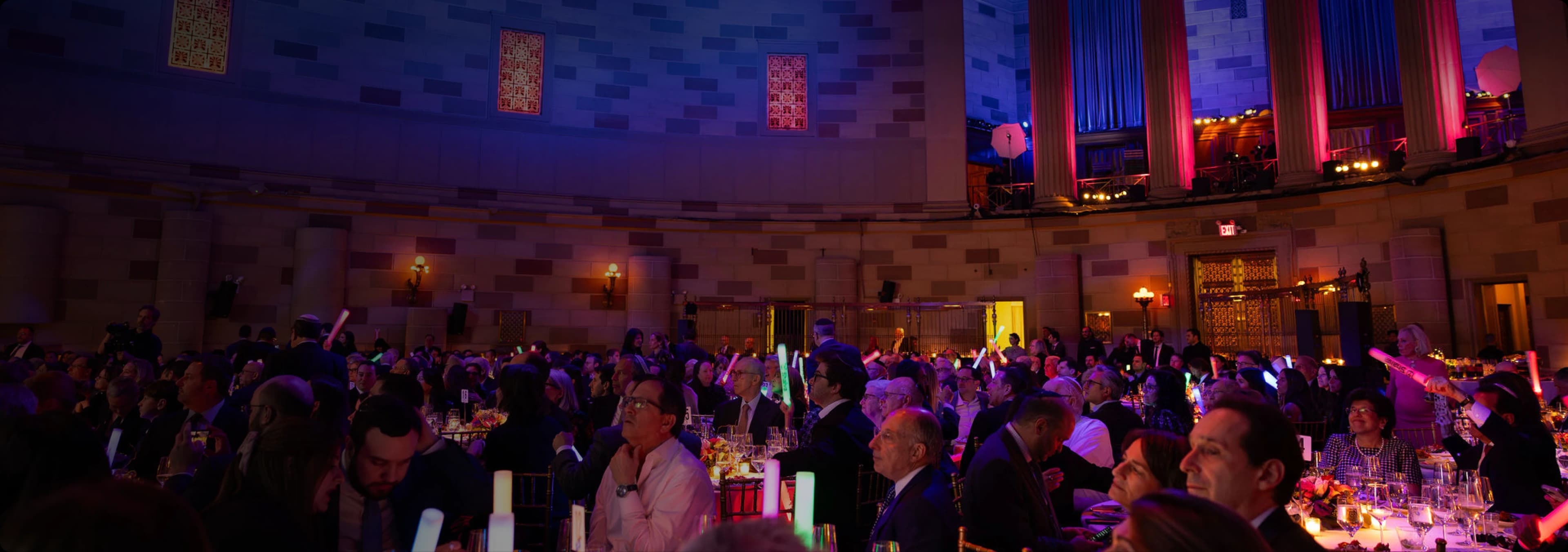 Black-tie gala guests at banquet tables under coloured lighting